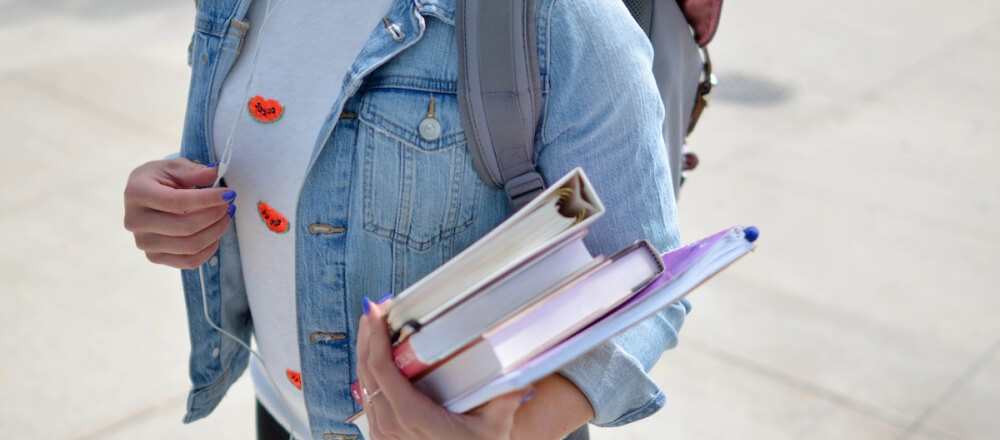 Female student walking with books in her hand and a backpack on.