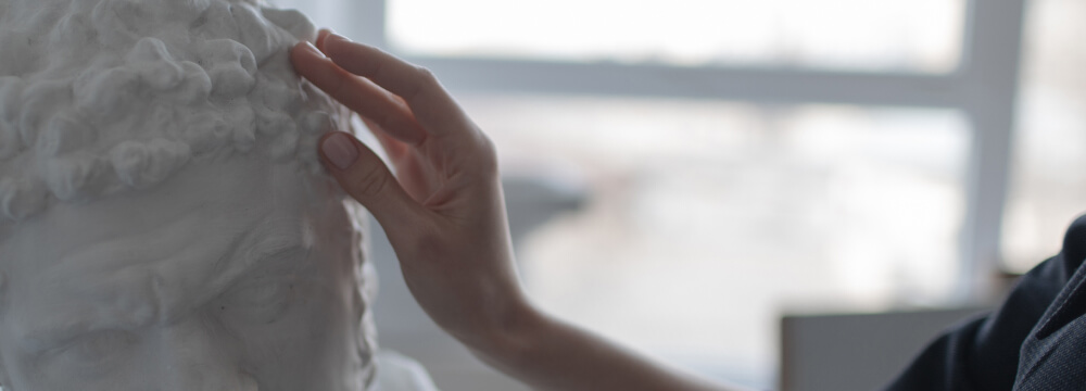 Hand touching a sculpture of ancient Greek man.